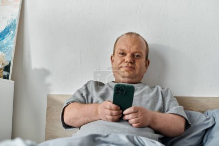 Ein Mann mit Inklusivität im Schlafzimmer, im Bett liegend und auf seinem Handy scrollend.