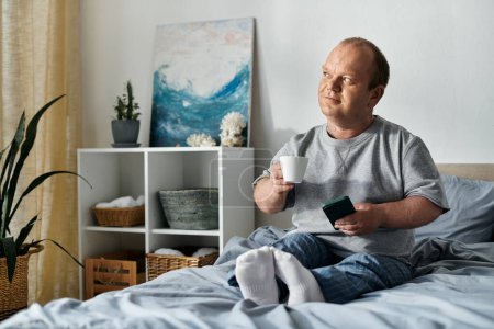 Ein Mann mit Inklusivität sitzt im Bett, genießt eine Tasse Kaffee und schaut aus dem Fenster und betrachtet vielleicht seinen Tag.
