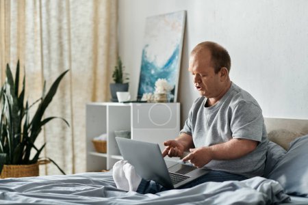 Un homme avec inclusivité est assis sur son lit, absorbé dans son ordinateur portable.