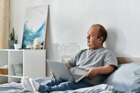 Ein inklusiver Mann sitzt mit seinem Laptop im Bett.