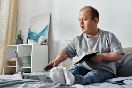 Un homme inclusif s'assoit dans son lit, travaille sur un ordinateur portable et tient un livre.