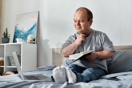 Un homme avec inclusivité est assis dans son lit, tenant soigneusement un cahier et un stylo, réfléchissant à sa journée.
