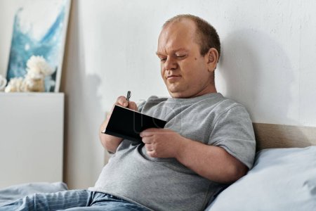 Un hombre con inclusividad se sienta en una cama, pluma en mano, reflexionando en su día mientras escribe en un cuaderno.