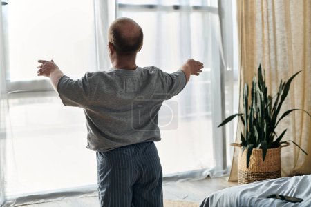 A man with inclusivity stretches in front of a window, arms outstretched, on a sunny morning.