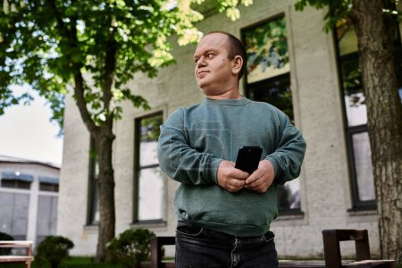Un homme avec inclusivité se tient devant un bâtiment, regardant réfléchi tout en tenant un téléphone.