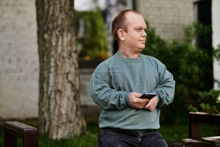 Ein inklusiver Mann sitzt auf einer Parkbank und hält ein Smartphone in der Hand.
