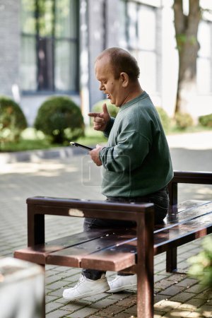 Un hombre con inclusividad se sienta en un banco en un parque de la ciudad, usando su teléfono.