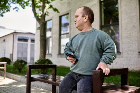 Ein inklusiver Mann sitzt auf einer Bank vor einem Gebäude und hält ein Telefon in der Hand..