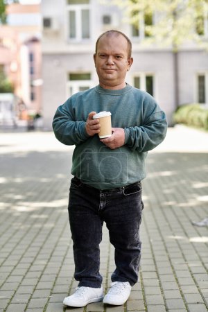 Un homme inclusif se tient dehors, tenant une tasse de café. Il sourit à la caméra.