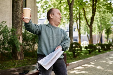 A man with inclusivity sits on a park bench, holding a coffee cup and a newspaper, enjoying the sunshine.