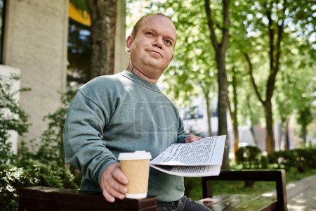 Un homme inclusif est assis sur un banc de parc, tenant un journal et une tasse de café, regardant contemplatif.