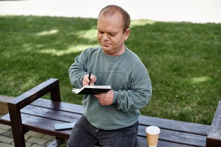 A man with inclusivity sits on a park bench writing in a notebook, enjoying a peaceful moment outdoors.