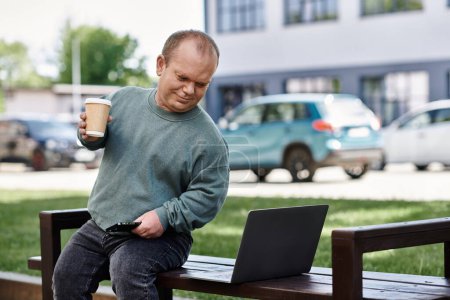 Un hombre con inclusividad se sienta en un banco en un parque de la ciudad, disfrutando de un café y usando su computadora portátil.