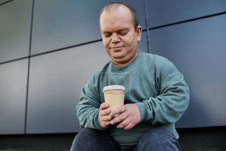 A man with inclusivity sits outside, thoughtfully holding a cup of coffee.