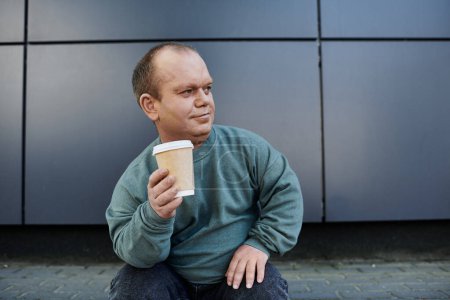 A man with inclusivity with a cup of coffee pauses for a moment, looking out over the city.