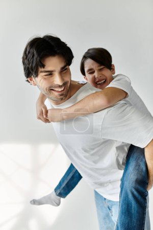 A father gives his son a piggyback ride, both laughing joyfully.