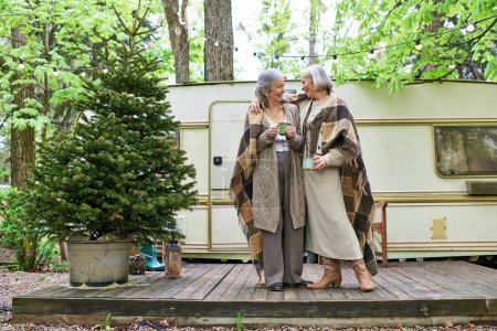 Ein lesbisches Paar genießt einen warmen Drink und einen Moment zusammen beim Zelten im Wald.