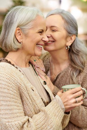 Photo for Two women, an older lesbian couple, are close together in a forest setting. They appear to be camping, and one of them is holding a mug. - Royalty Free Image