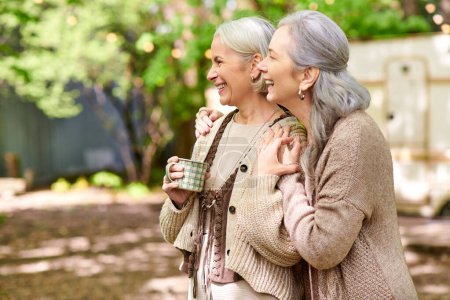 Zwei Frauen mittleren Alters lachen zusammen bei einer Tasse Kaffee während eines Campingausflugs.