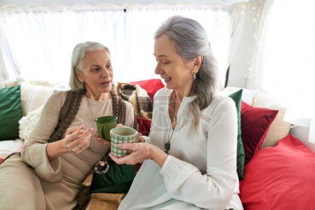 Zwei Frauen mittleren Alters, ein lesbisches Paar, sitzen in einem Wohnmobil, genießen ihre Tassen Tee und Gesellschaft voneinander.