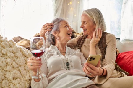 Dos mujeres de mediana edad, una pareja lesbiana, comparten una copa de vino y un momento acogedor dentro de su casa rodante durante un viaje por carretera.