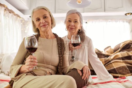 A lesbian couple enjoys a glass of wine inside their RV during a road trip.