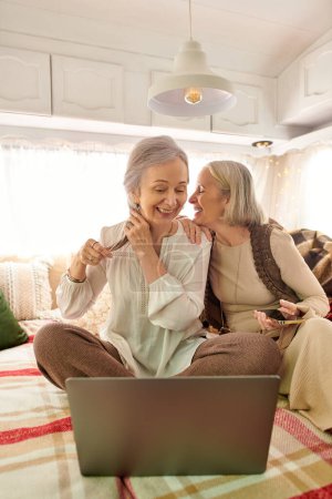 Two middle-aged women laugh and share a moment inside their camping van.