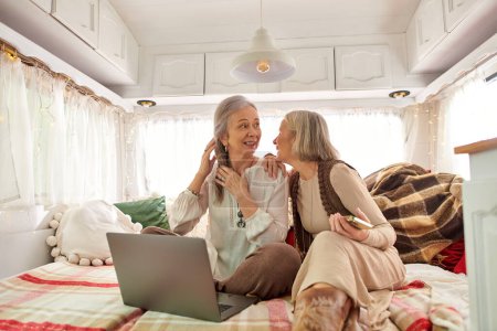 Two middle-aged women are cozy and relaxed inside of a camper van, enjoying a road trip together.