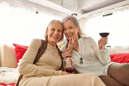 Ein lesbisches Paar lächelt und lacht, während es ein Glas Wein in einem Wohnmobil genießt.