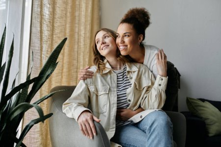 Deux femmes, un couple lesbien diversifié, s'assoient ensemble sur un canapé à la maison, profitant d'un moment d'intimité et d'affection.