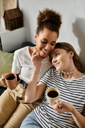 Una pareja lesbiana disfruta de una acogedora mañana juntos en casa, compartiendo café y tierno afecto.
