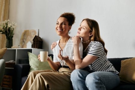 Ein lesbisches Paar entspannt auf einer Couch zu Hause, genießt eine Tasse Kaffee und ein Gespräch.