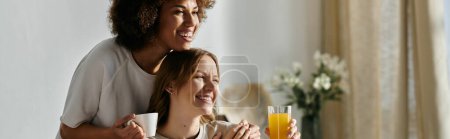 Photo for A lesbian couple enjoying each others company at home, with one holding a mug and the other holding a glass of juice. - Royalty Free Image