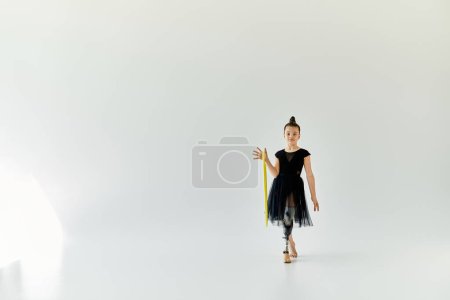 A young girl with a prosthetic leg practices gymnastics with a yellow hoop in a white studio.