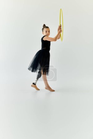 A young girl with a prosthetic leg practices gymnastics with a hula hoop in a studio setting.