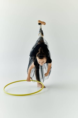 A young girl with a prosthetic leg practices her gymnastics routine with a hula hoop in a studio.