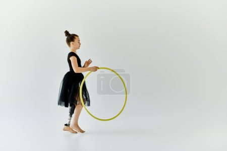 A young girl with a prosthetic leg practices gymnastics with a hula hoop in a white studio.