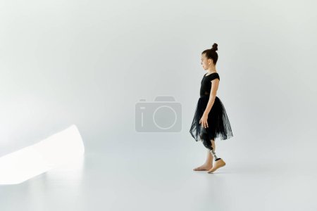 Una joven en un maillot negro y tutú se encuentra en un estudio blanco, mostrando su fuerza y gracia mientras usa una pierna protésica.