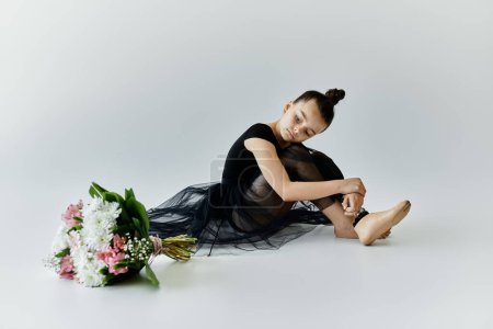 A young girl wearing a black tutu sits on a white floor, her prosthetic leg resting beside her.