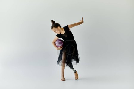 A young girl with a prosthetic leg performs a gymnastics routine with a purple ball.