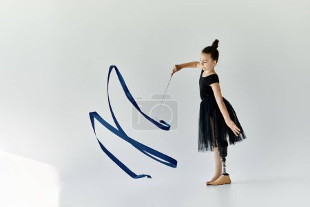 A young girl with a prosthetic leg practices rhythmic gymnastics, skillfully manipulating a blue ribbon.