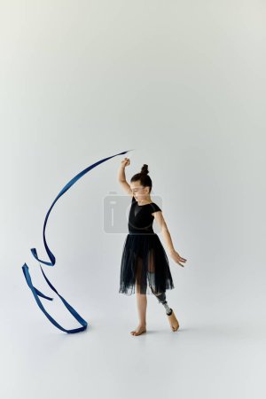 A young girl with a prosthetic leg gracefully performs a gymnastics routine with a blue ribbon.