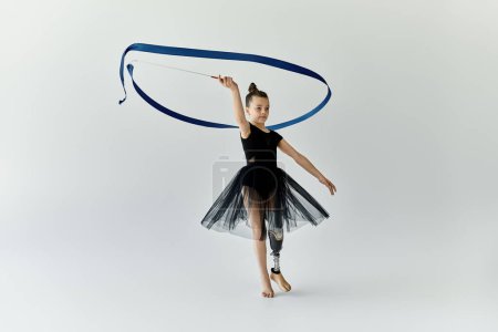 A young girl with a prosthetic leg performs a rhythmic gymnastics routine with a blue ribbon.