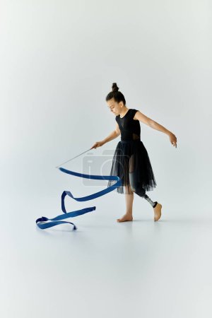 A young girl with a prosthetic leg performs gymnastics with a blue ribbon.