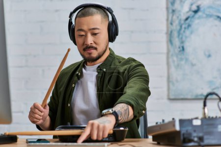 A handsome Asian man wearing headphones plays drums in a studio setting.