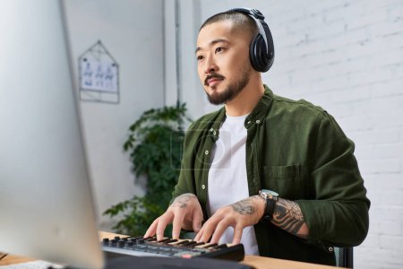 An Asian man with headphones plays a keyboard in his studio.