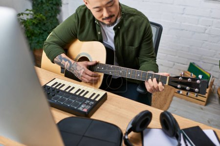 A man plays an acoustic guitar while sitting in a music studio.