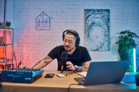 A handsome Asian man recording a podcast in his colorful home studio.