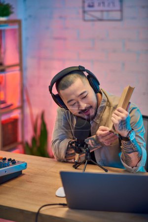 An Asian man records a podcast in his studio.