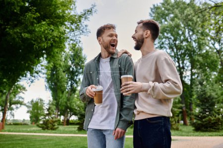 A gay couple walks through a green park, laughing and holding coffee.
